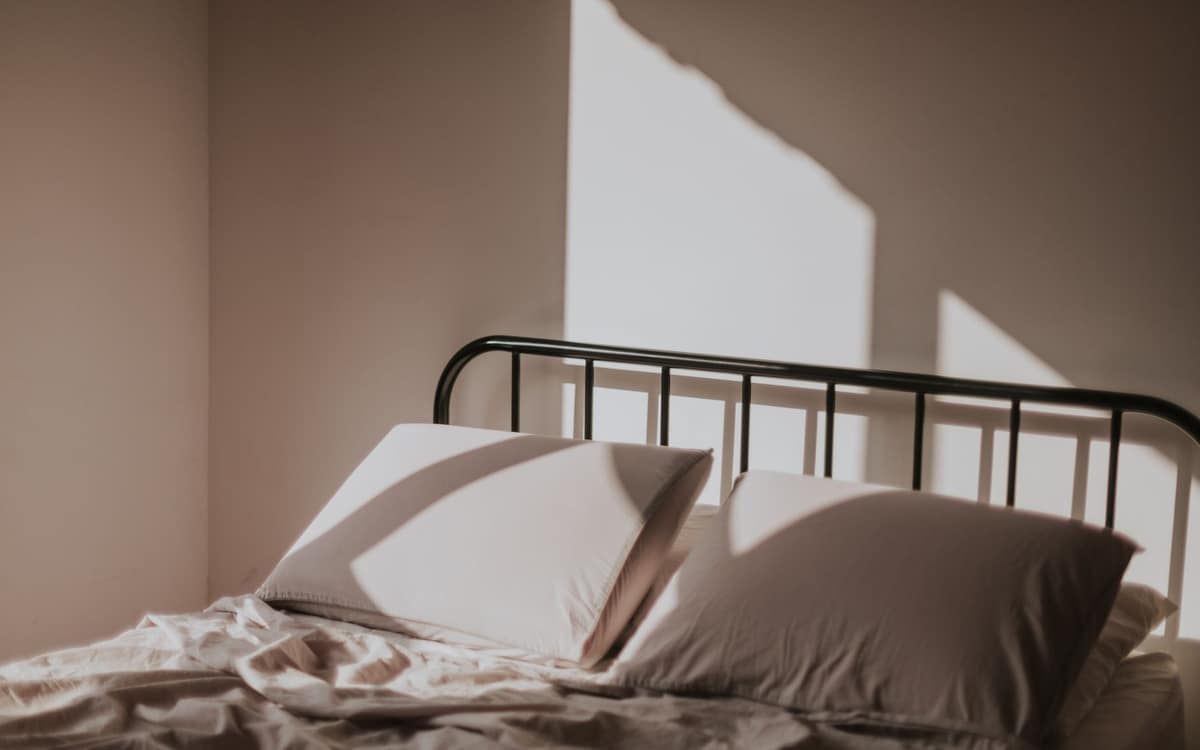 A neatly made bed in white linen in soft morning light